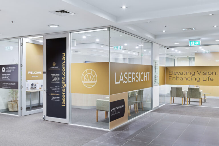A modern LASERSIGHT eye surgery clinic with glass walls, gold and white branding, seating area with chairs and tables, and welcoming signage reading “Elevating Vision, Enhancing Life”.