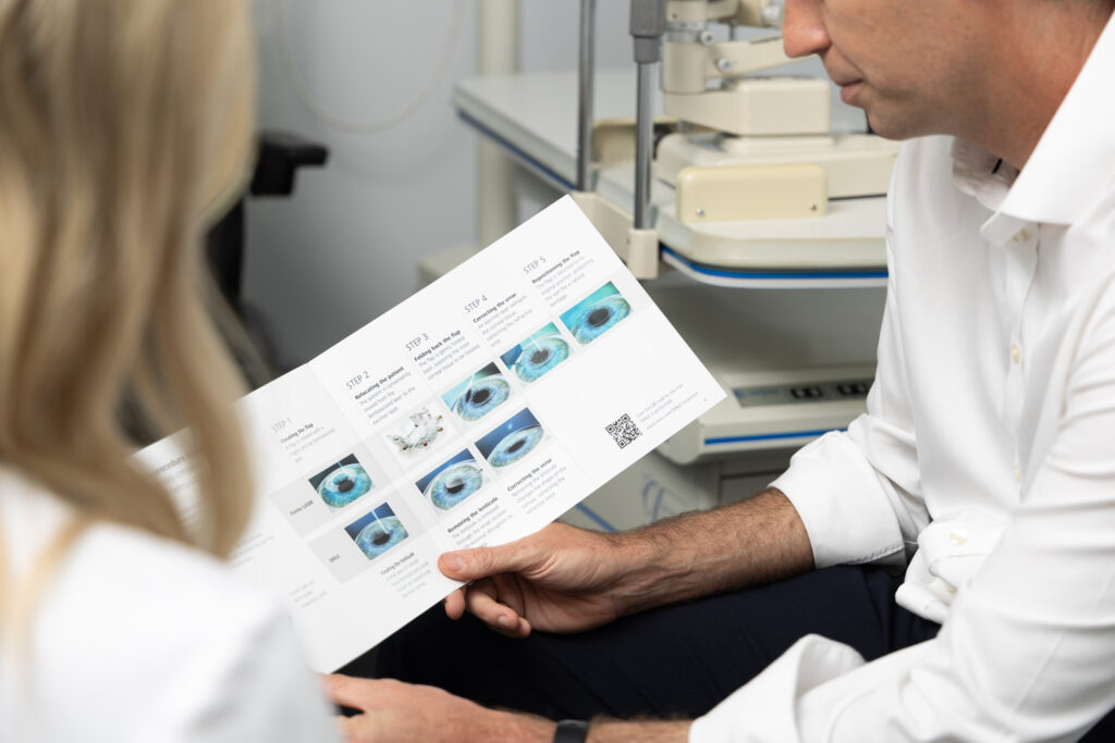 A man and a woman in Dr Brett Drury's surgery review a brochure with eye images and explanatory text, likely discussing eye health or treatment options during a consultation.