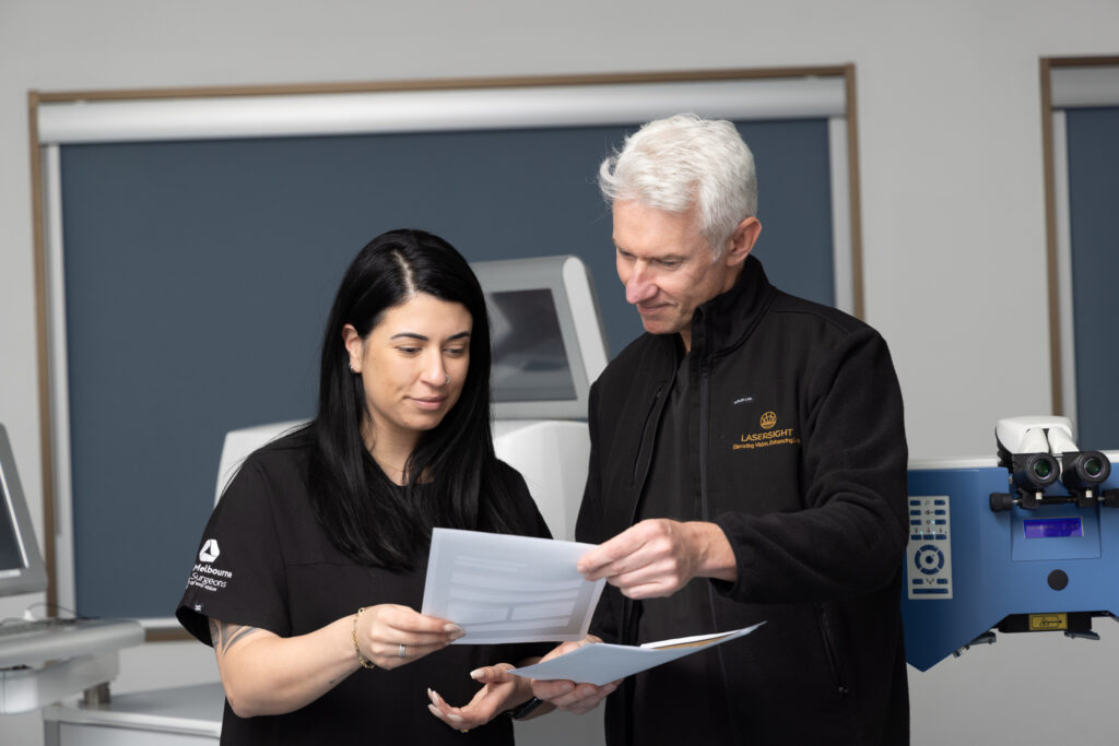 Dr Dermot Cassidy and a colleague in professional attire examine documents together in a modern office or medical setting with technical equipment in the background.